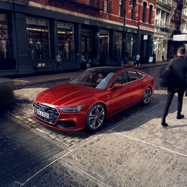 Red car parked on urban street with pedestrians and storefronts.