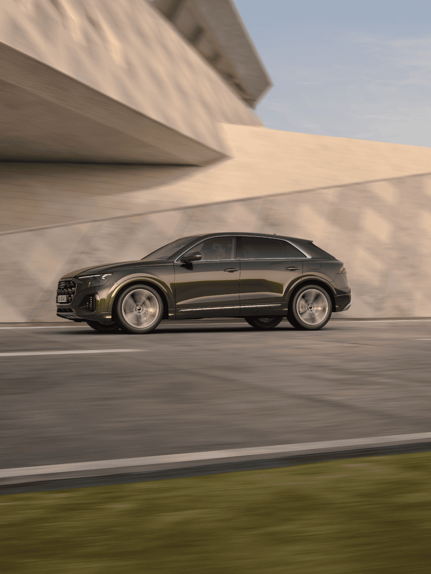 Audi Q8 tfsi e moving along road approaching modern bridge.