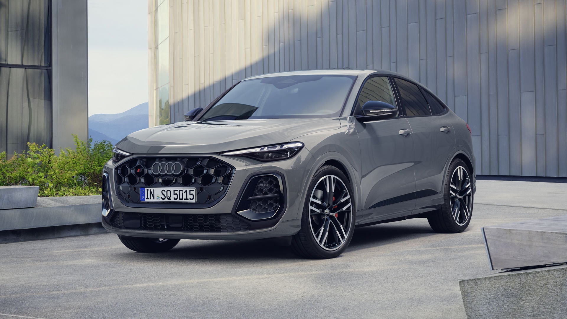 Der SQ5 Sportback steht im schrägen Frontprofil vor einem großen Gebäude. Das Fahrzeug ist Nardograu lackiert.