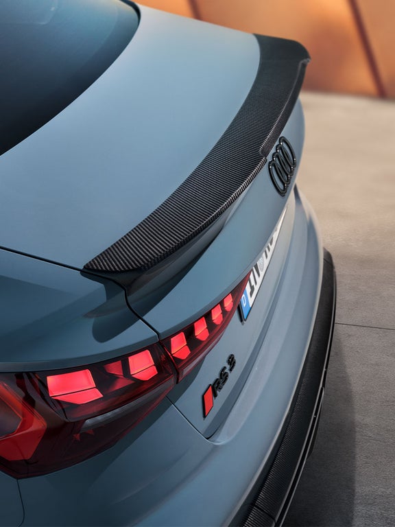Heckansicht einer Audi RS 3 Limousine mit schwarzem Carbonfaser-Spoiler auf der Kofferraumklappe und leuchtenden Rücklichtern.