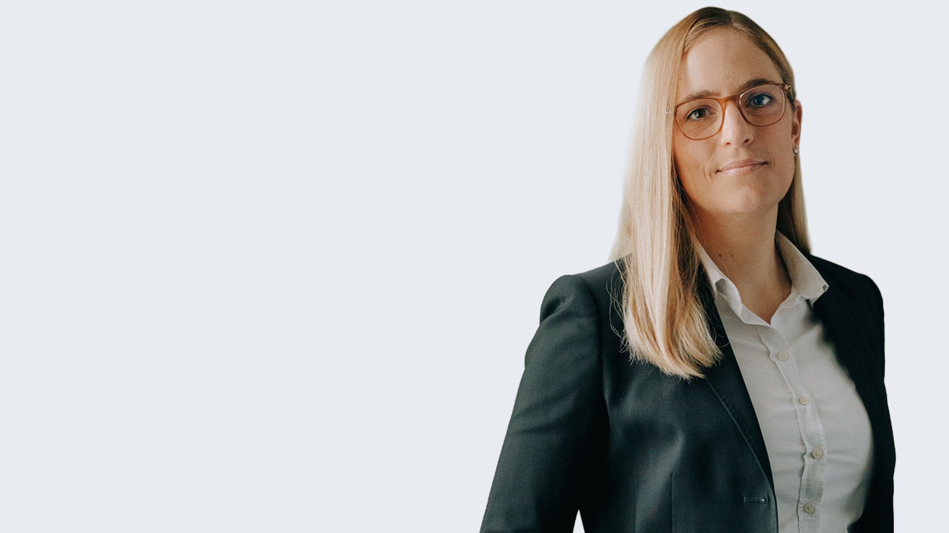 Porträt einer Frau mit langen blonden Haaren, Brille und Business-Outfit vor hellem Hintergrund, Blick in die Kamera.