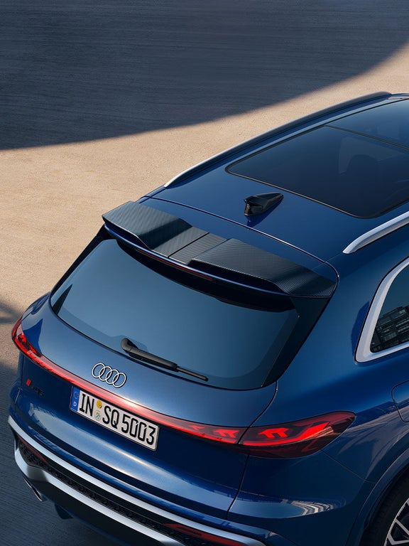 Ein blauer Audi SQ5 SUV mit Carbon-Spoiler von schräg oben fotografiert, geparkt auf hellem Betonboden.