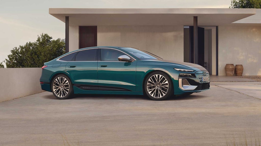 Seitenansicht eines grünen Audi S6 Sportback e-tron vor hellem Gebäude, mit Fokus auf das elegante Fahrzeugprofil.
