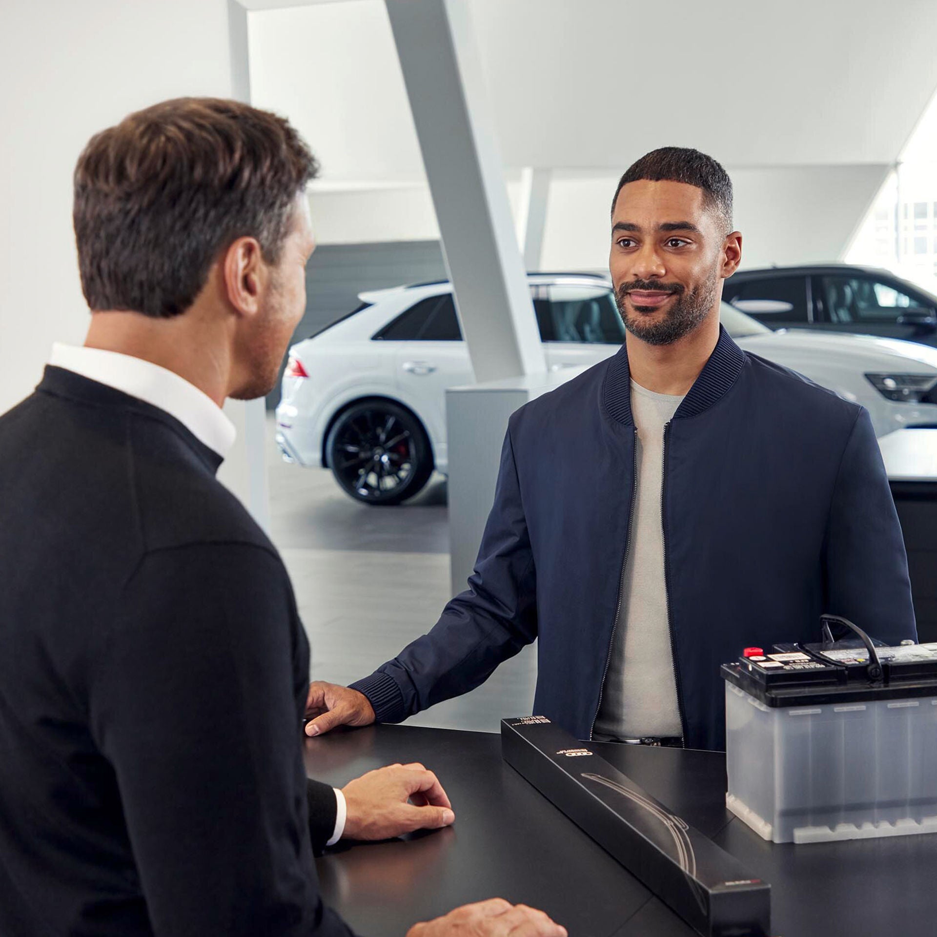 Ein Mann kauft Zubehörartikel von Audi, welche auf einem Verkaufstresen liegen, an dem ein Verkäufer steht