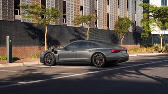 A grey sedan parked beside a charging station on an urban street.