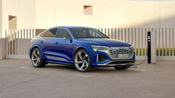 Blue Audi electric vehicle charging at a station with modern architecture in the background