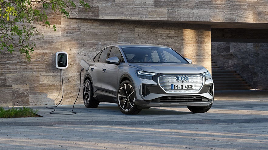Flottenfahrzeug Q4 Sportback e-tron lädt an Audi Wallbox auf vor einer modernen Hauswand