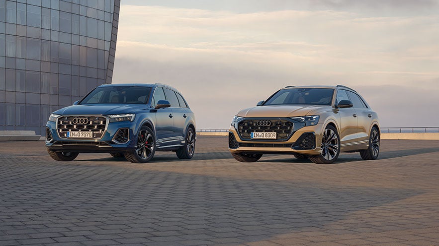 Außenansicht Flottenfahrzeuge Q7 und Q8 auf einem Parkplatz, links sieht man ein modernes Gebäude.