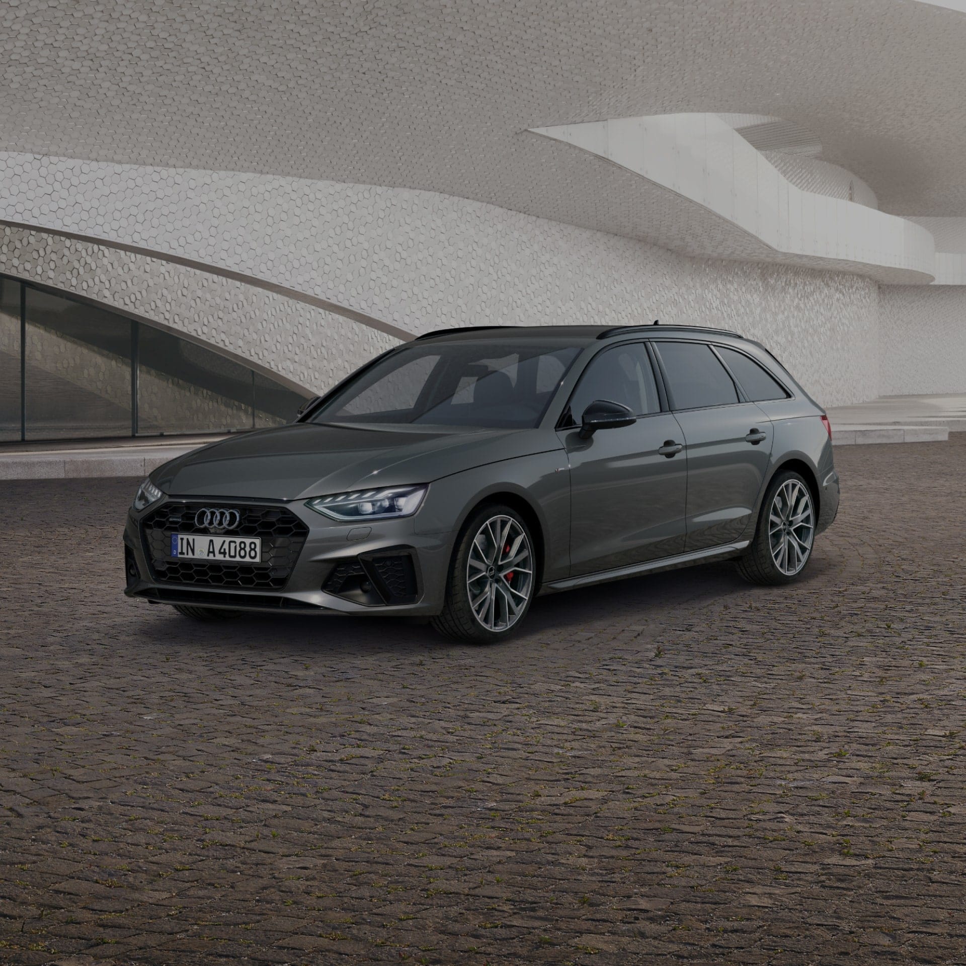 A grey car parked in front of a modern textured building facade.