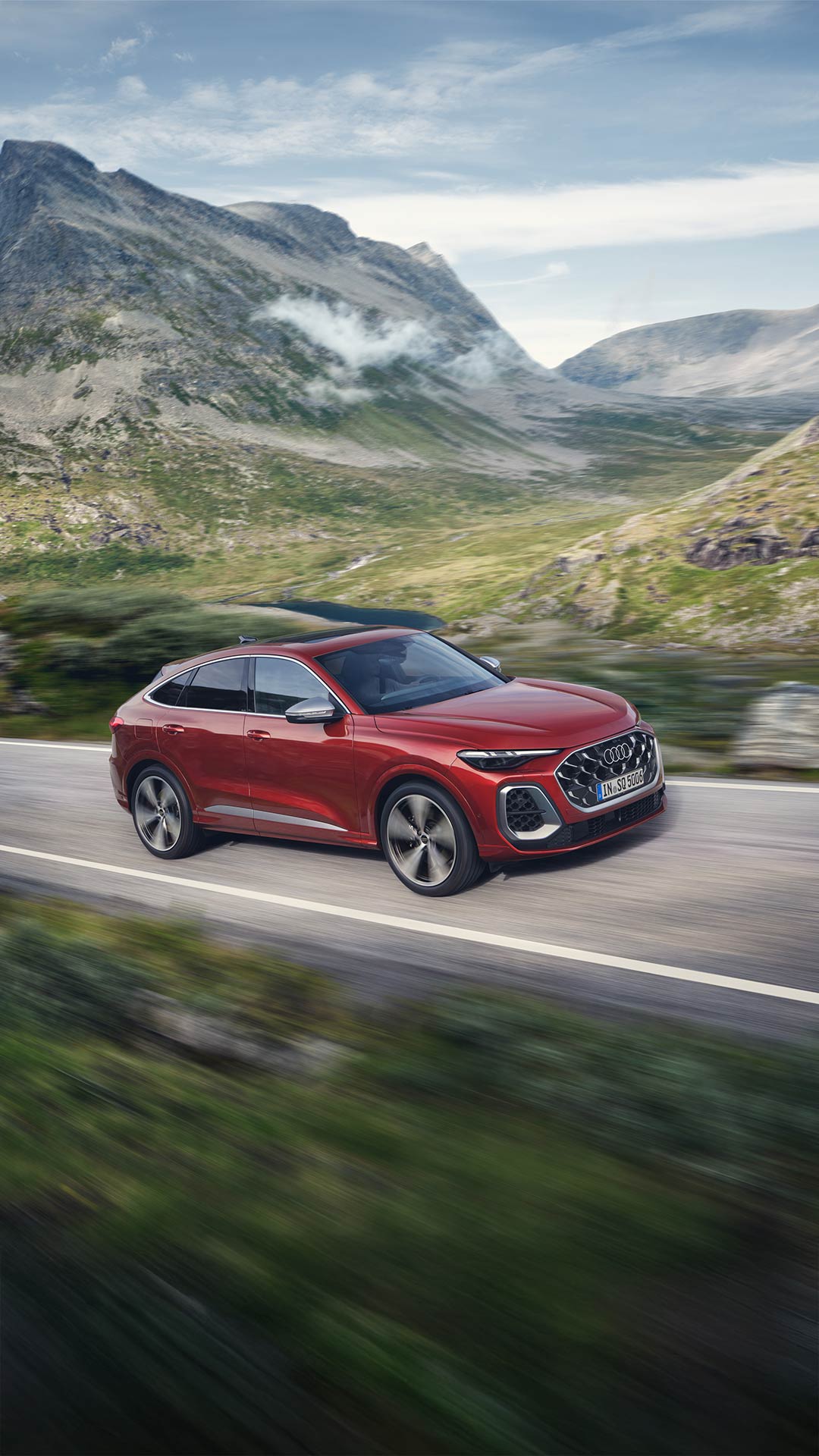 Ein roter Audi SQ5 Sportback fährt bei Tageslicht auf einer kurvigen Landstraße durch grüne Hügellandschaft.