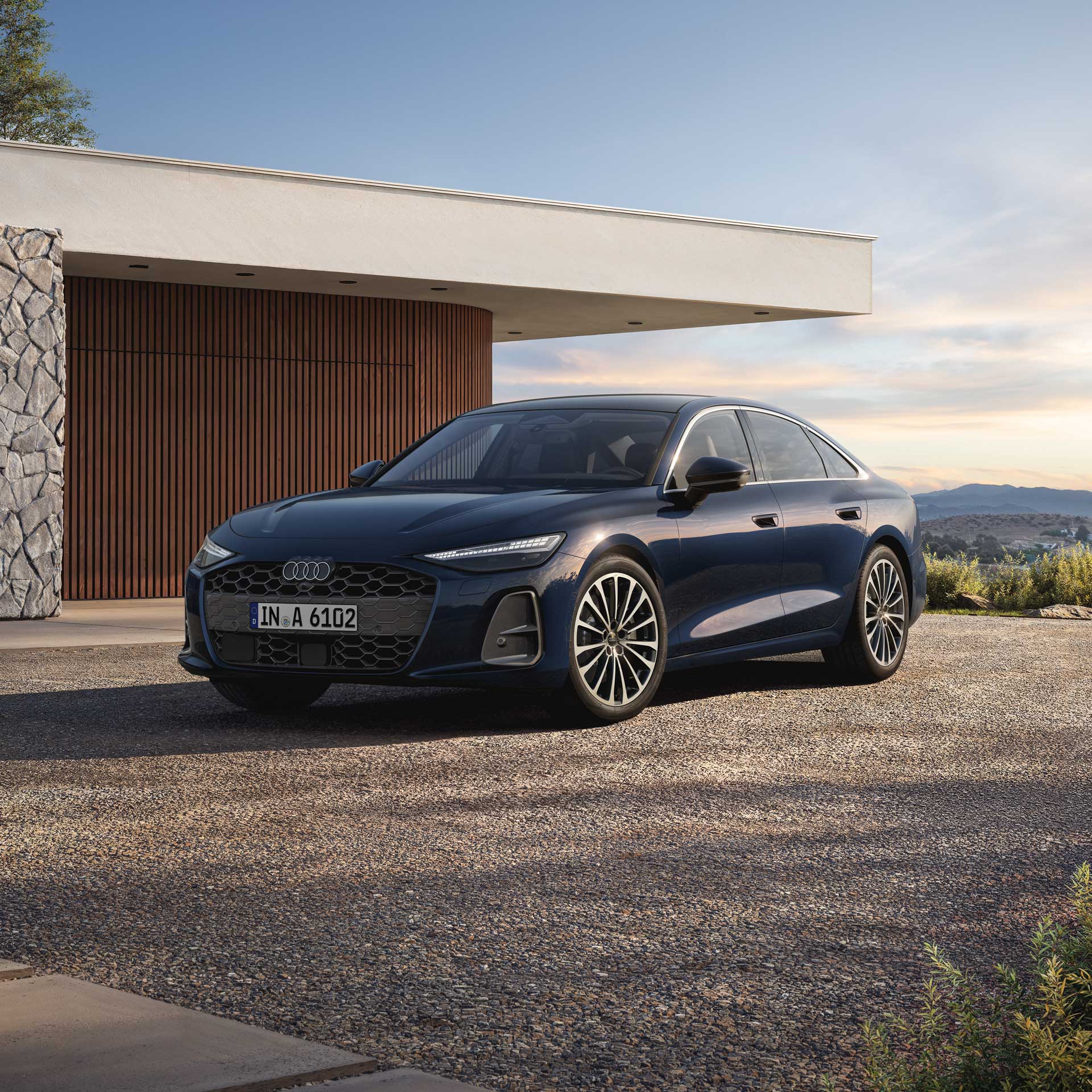 Dunkelblaue Audi A6 Limousine steht vor einem modernen Gebäude mit Holzfassade und Naturstein bei Tageslicht.