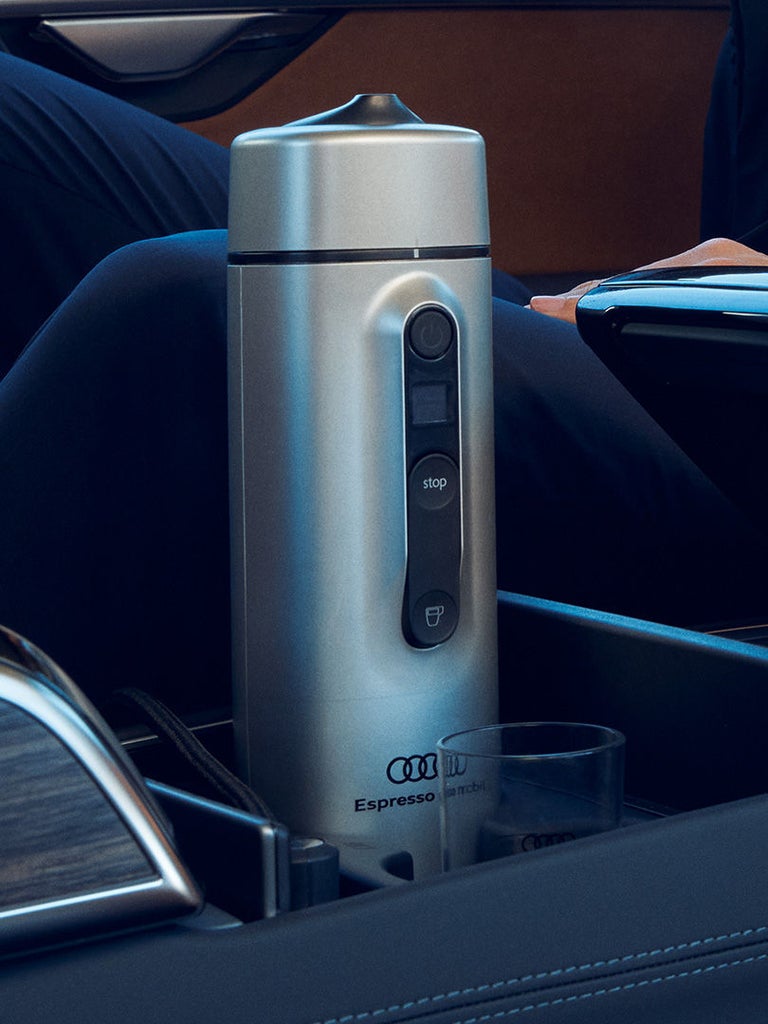 Silberne Espressomaschine in der Mittelkonsole eines Audi, neben einer Person im Anzug.