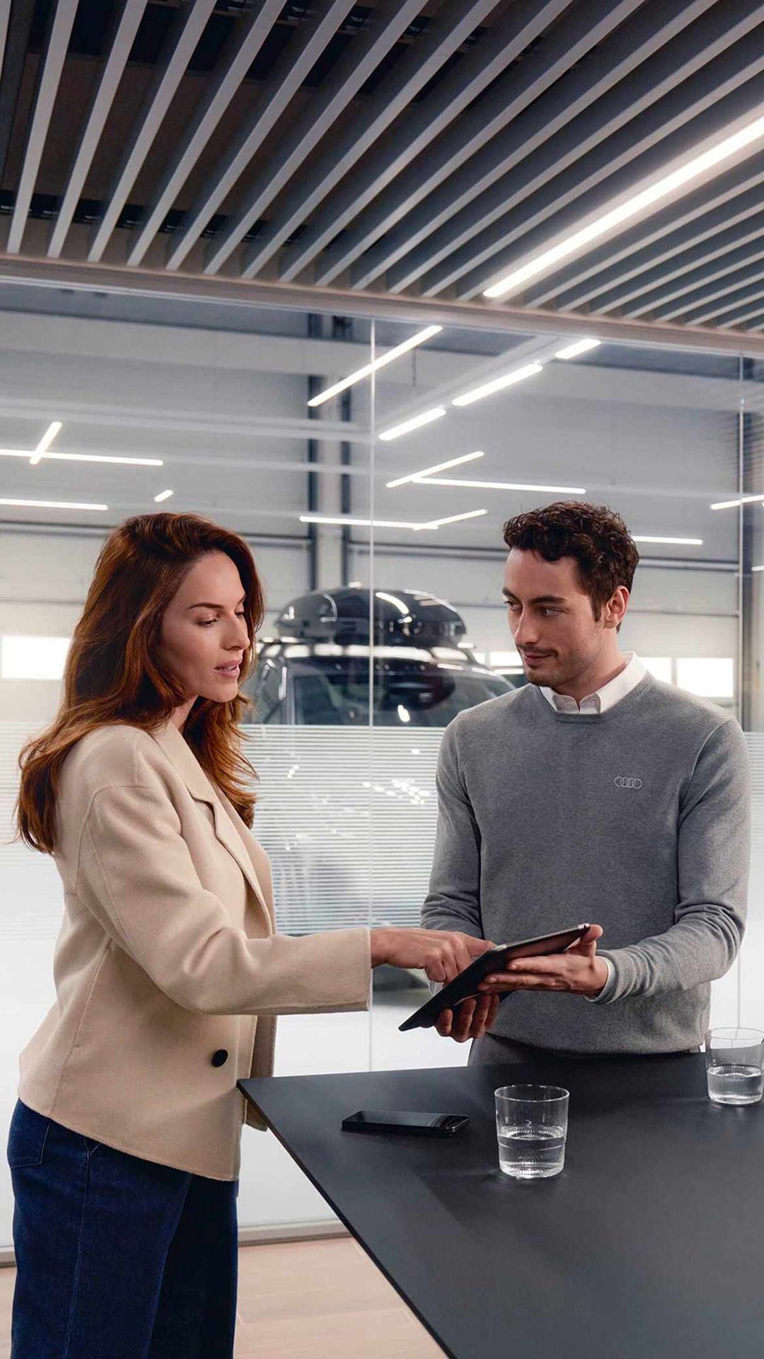 Consulente Audi che mostra a cliente Audi i piani di manutenzione su tablet in concessionaria