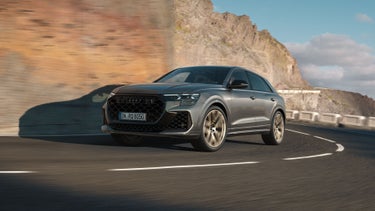 Der RS Q8 SUV schräg von vorne in einer Kurve auf einer Bergstraße. Das Fahrzeug wirft Schatten an die rechts aufragende Bergwand.