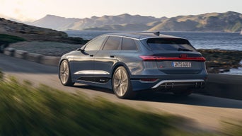 Grauer Audi S6 Avant e-tron fährt auf einer Küstenstraße, Meer und Berge im Hintergrund.