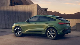 Grüner Audi Q5 Sportback steht vor modernem Betongebäude bei tief stehender Sonne. Hinter dem Gebäude sind Berge zu sehen.