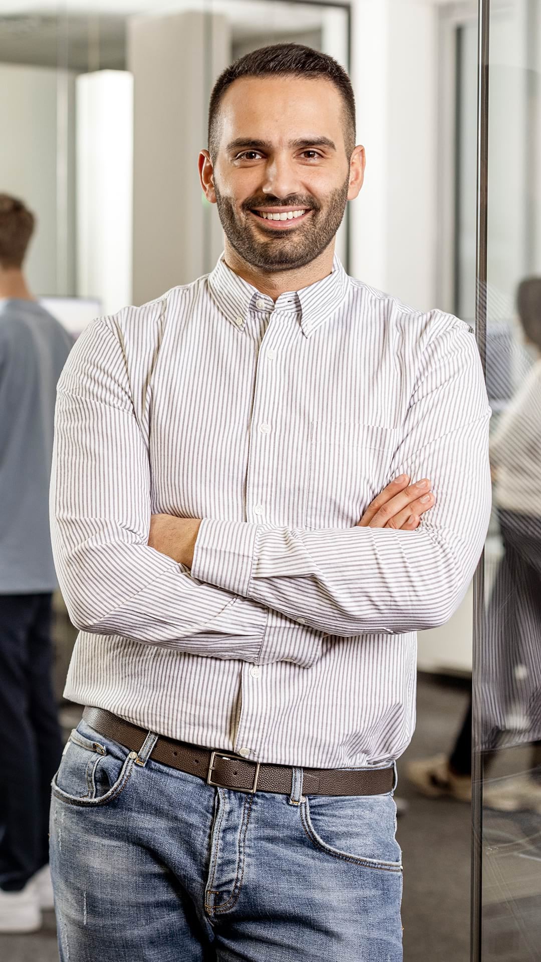 Junge Frau mit kurzem Haaren sitzt auf einer Mauer vor einem Meer und schaut zur Seite