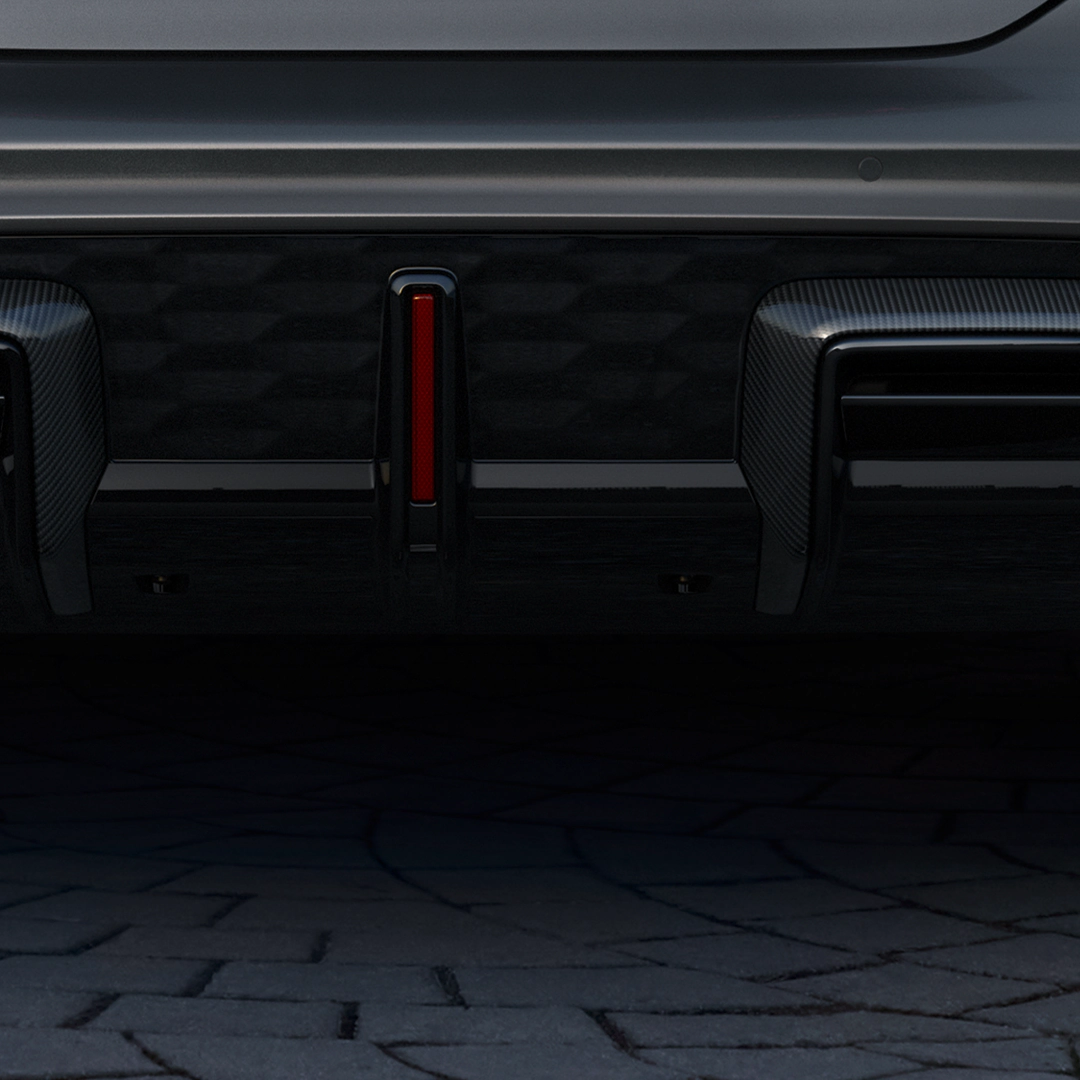 Rear car bumper with red reflector, carbon fibre trim, on a brick surface.