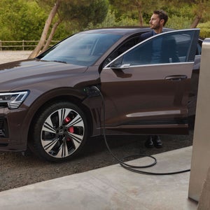 A man behind an open door of a brown Audi while it's connected to an EV charger