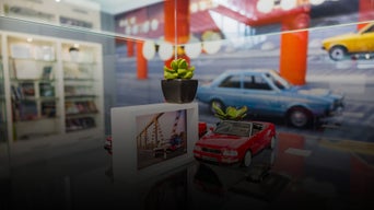 Autoausstellung mit roten Modellautos, Pflanze und großformatigen Bildern verschiedener Fahrzeuge.