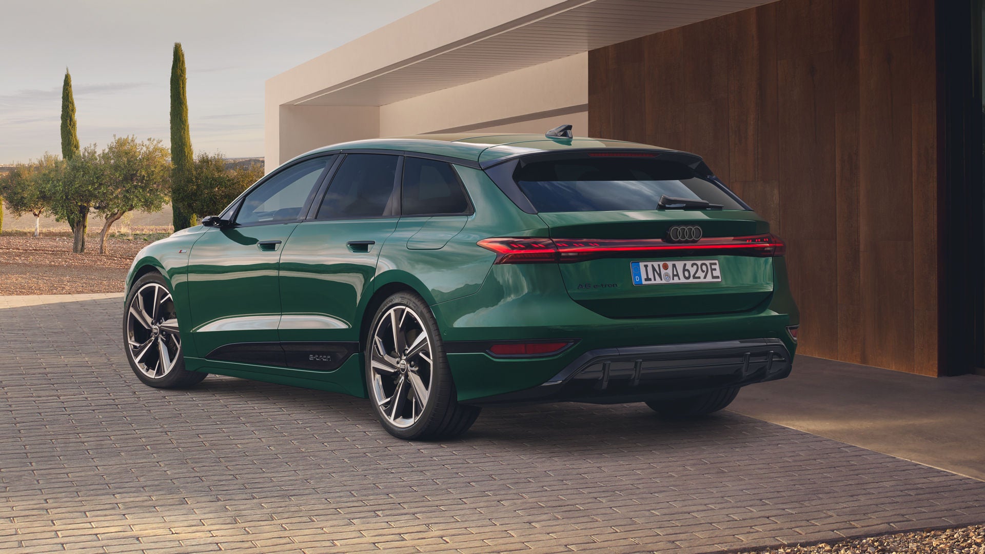Der Audi A6 Avant e-tron mit Individuallackierung Audi exclusive Goodwoodgrün Perleffekt, schräg von hinten fotografiert, parkt vor einem modernen Wohngebäude.