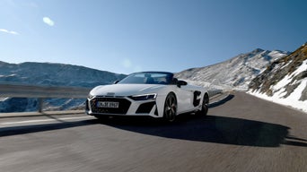 Weißer Audi R8 Spyder V10 performance quattro fährt in den Bergen bei sonnigem Wetter mit blauem Himmel.