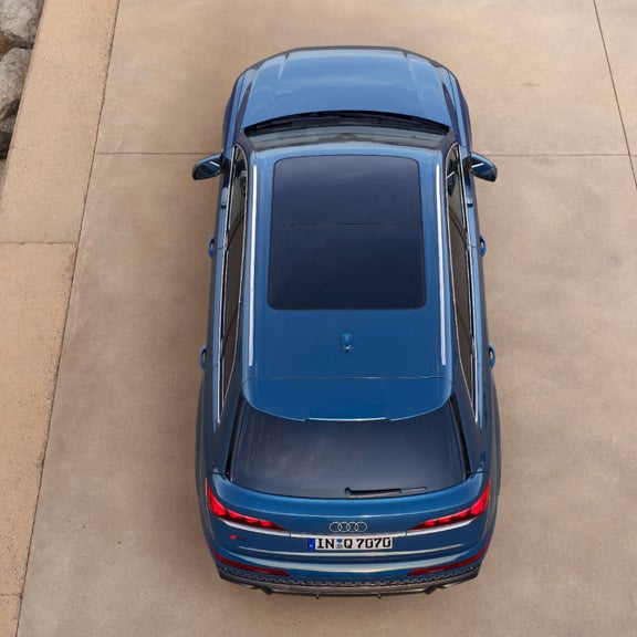 Aerial view of a parked car with a sunroof, casting a shadow on a concrete surface.