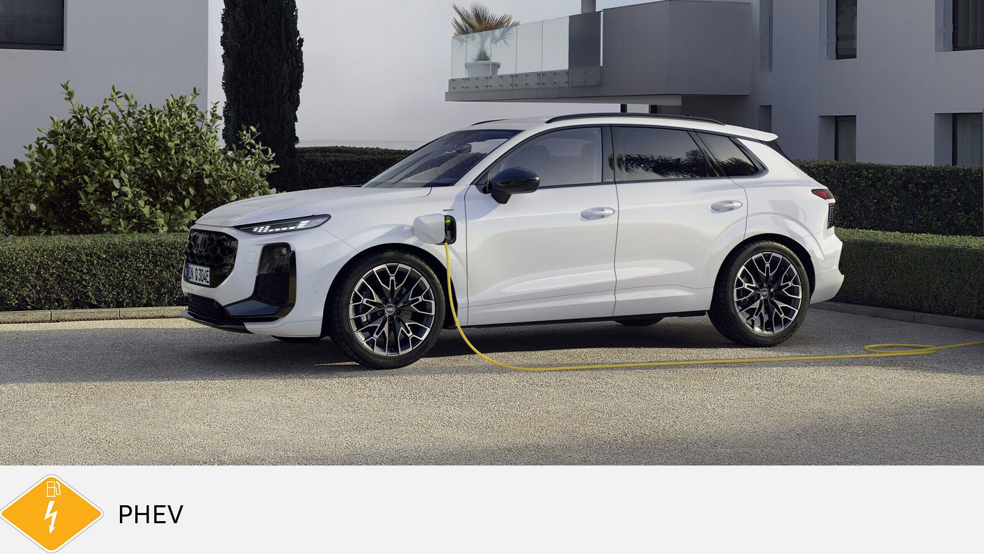 White Audi Q3 plug-in hybrid in side view charging with yellow cable in front of modern building in daylight. Yellow PHEV symbol with fuel pump below.