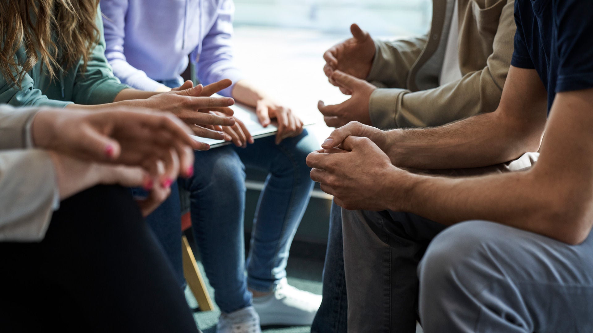 Several people sit in a circle and gesticulate during a conversation; the focus is on their hands.