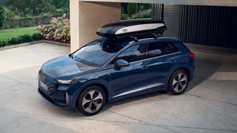 Audi Q4 e-tron en bleu foncé avec coffre de toit, garé dans l'allée d'une résidence haut de gamme avec jardin verdoyant en arrière-plan.