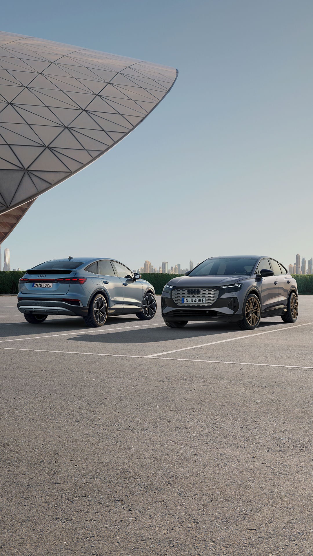 Two Audi SUVs parked with a city skyline in the background at dusk.