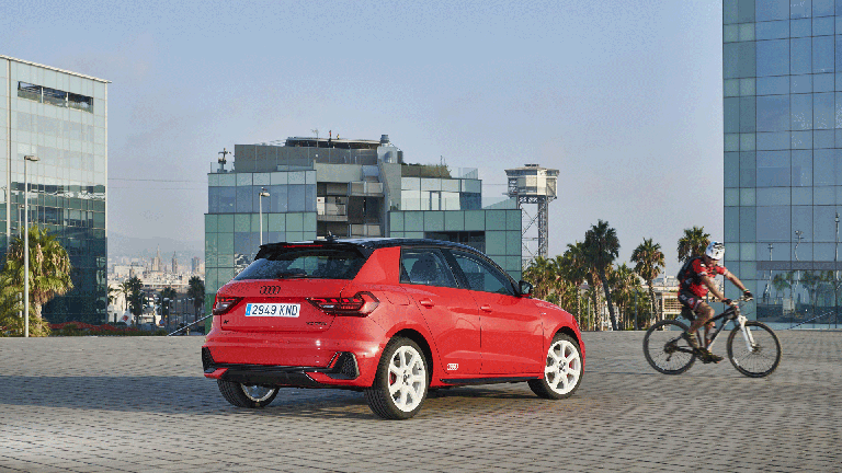 Roter Audi A1 steht zwischen modernen Glasgebäuden, Radfahrer fährt rechts vorbei.