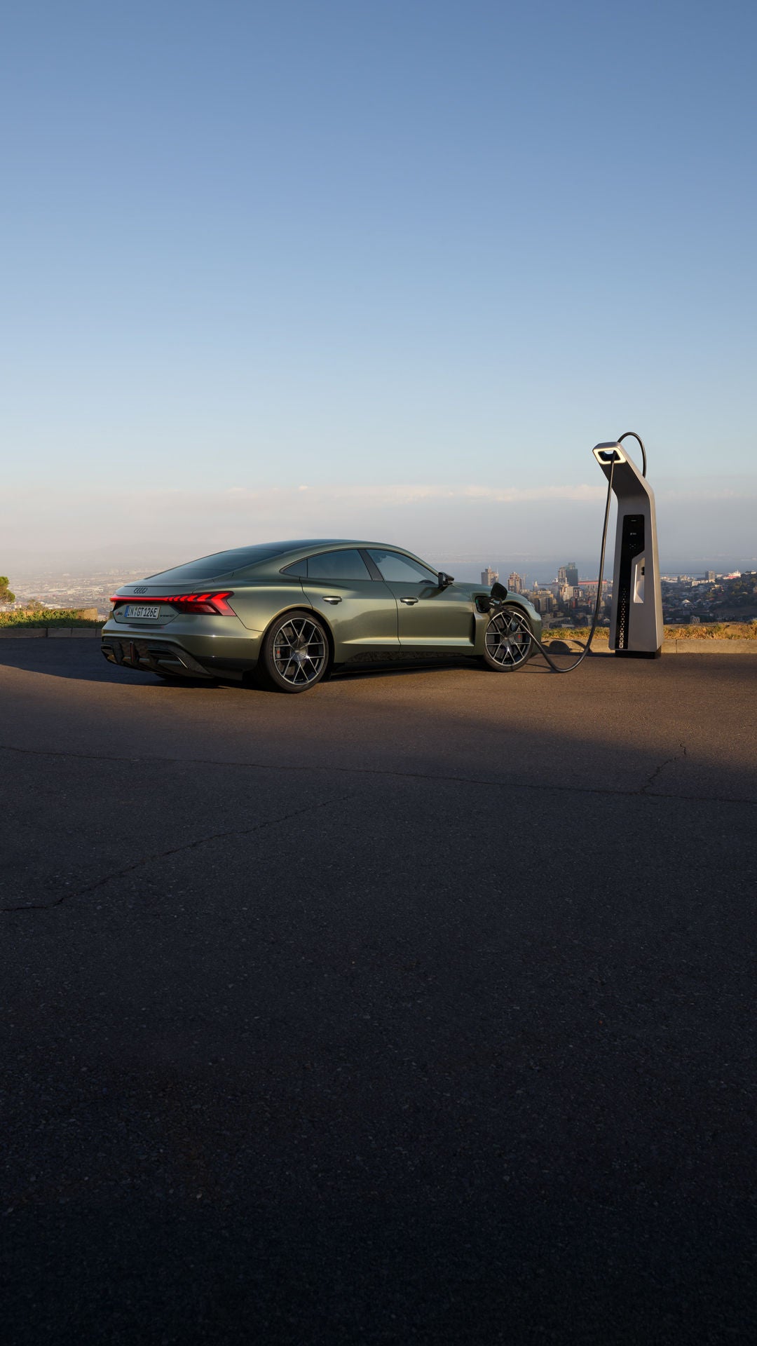 Grüner Audi RS e-tron GT performance lädt an einer Schnellladestation mit Stadtblick im Hintergrund.
