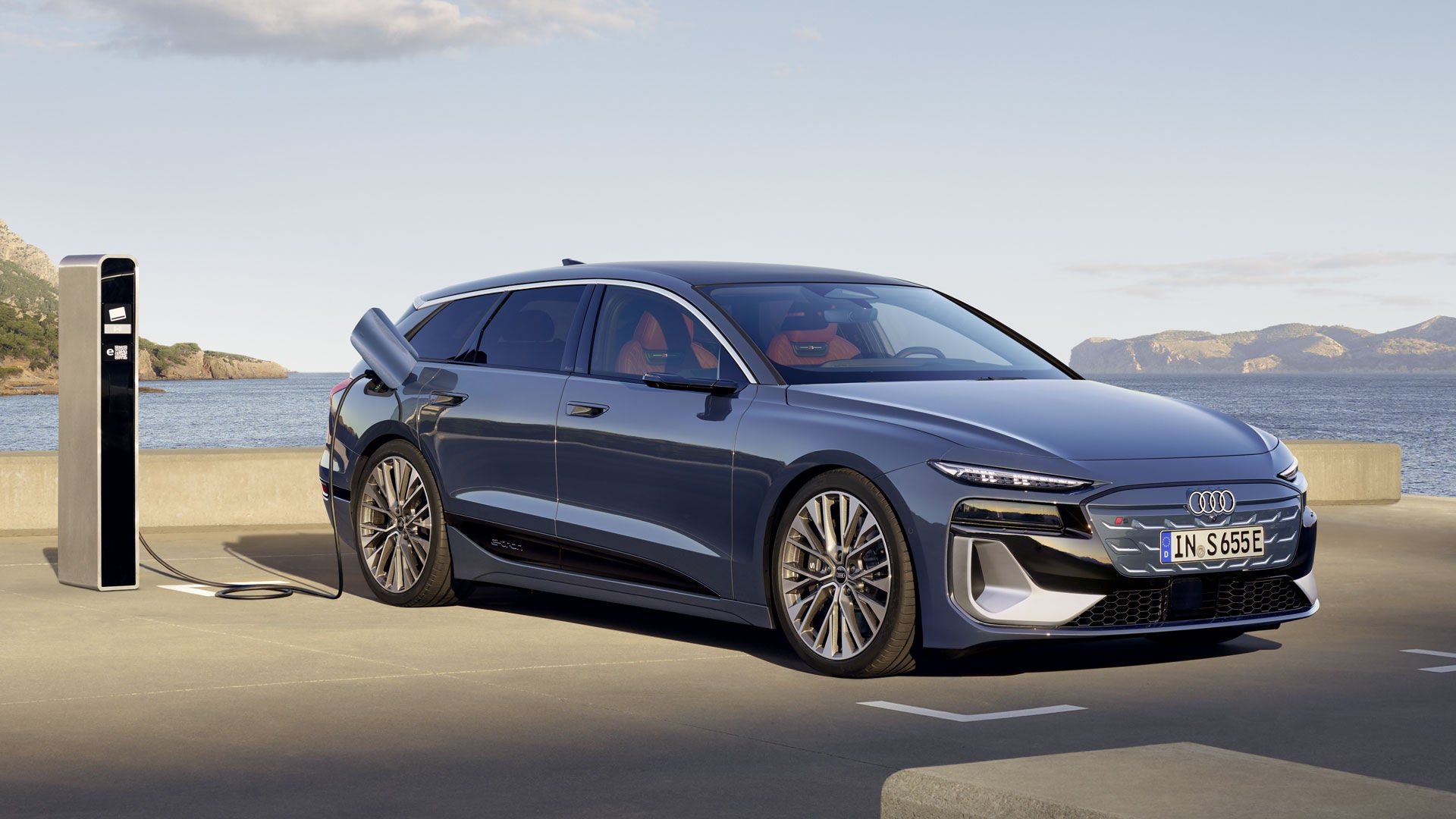 S6 Avant e-tron står parkerad vid en laddstation. Hav och berg i bakgrunden.