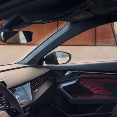Interior view of a Audi RS3 Saloon car showcasing the dashboard, steering wheel, and side mirror.