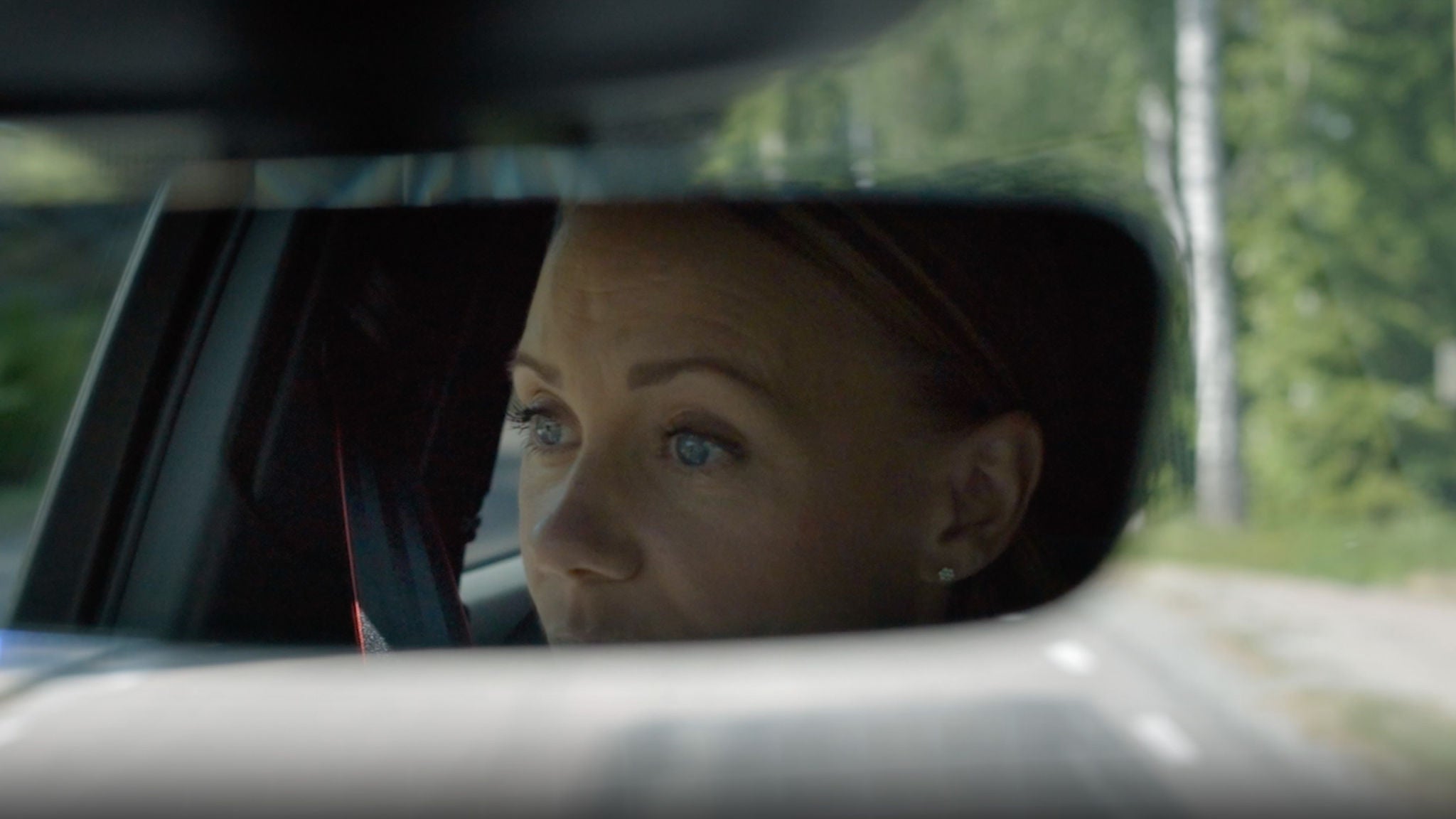 Frida Hansotter kör en Audi på en landsväg och syns i backspegeln.