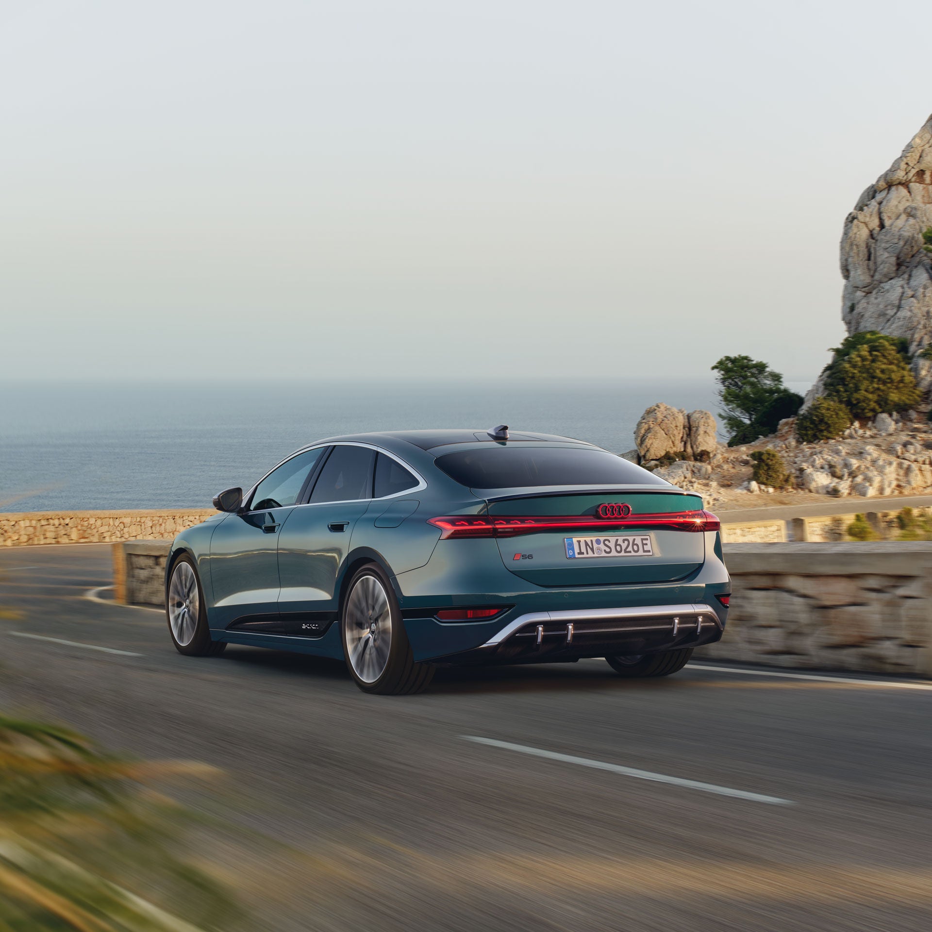 Ein blauer Audi fährt auf einer Küstenstraße.