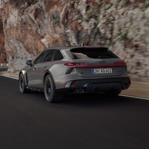Dynamische Fahraufnahme eines beigegrauen A6 allroad in Dreiviertel Heckansicht auf einer Gebirgsstraße.