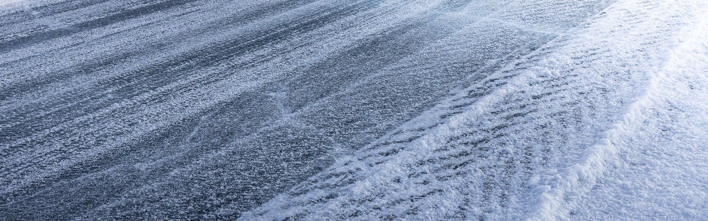 Strukturierte, vereiste Straße mit Reifenspuren und Schnee an der Seite.