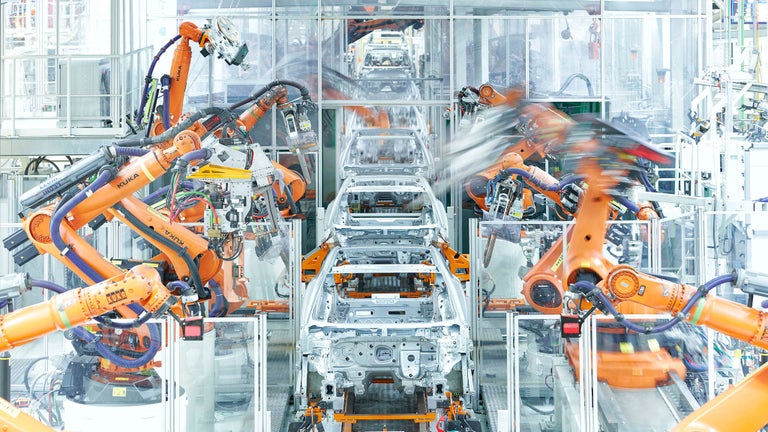 Produktionsstraße mit orangenen Industrierobotern, die silberne Fahrzeugkarosserien montieren.