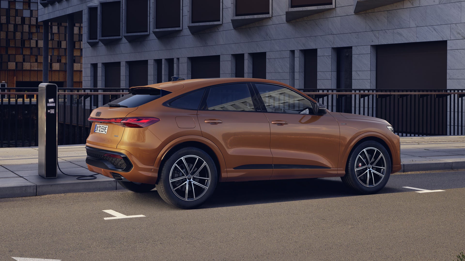 Der Q5 Sportback mit der Individuallackierung Ipanemabraun Metallic steht auf einer Brücke und ist an eine Ladestation angeschlossen.