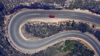 Extreme Vogelperspektive eines roten Autos, das durch eine bergige Serpentinen-Landschaft fährt.