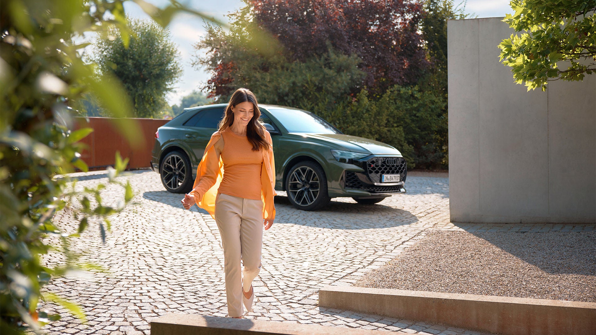 A woman runs energetically alongside a green SUV and smiles.