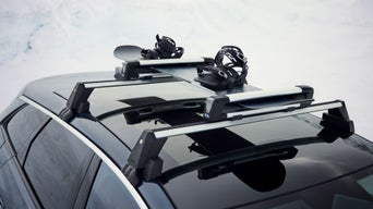 Snowboard mit Bindungen auf Dachträger eines Audi im Schnee befestigt.