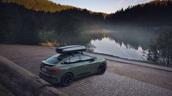Audi Q4 e-tron Sportback vert avec coffre de toit, garé au bord d’un lac, entouré d’une forêt et d’une eau calme reflétant le paysage.