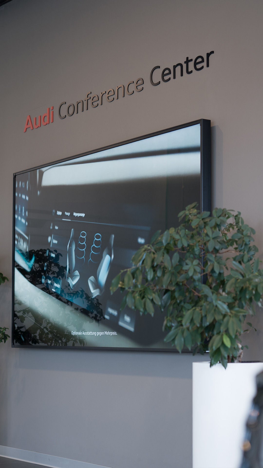 Wand mit Schriftzug „Audi Conference Center“, Bildschirm und zwei Pflanzen im Eingangsbereich.