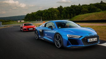 Blue and red Audi R8 Coupé drive behind each other on a race track, the blue Audi R8 drives in front.
