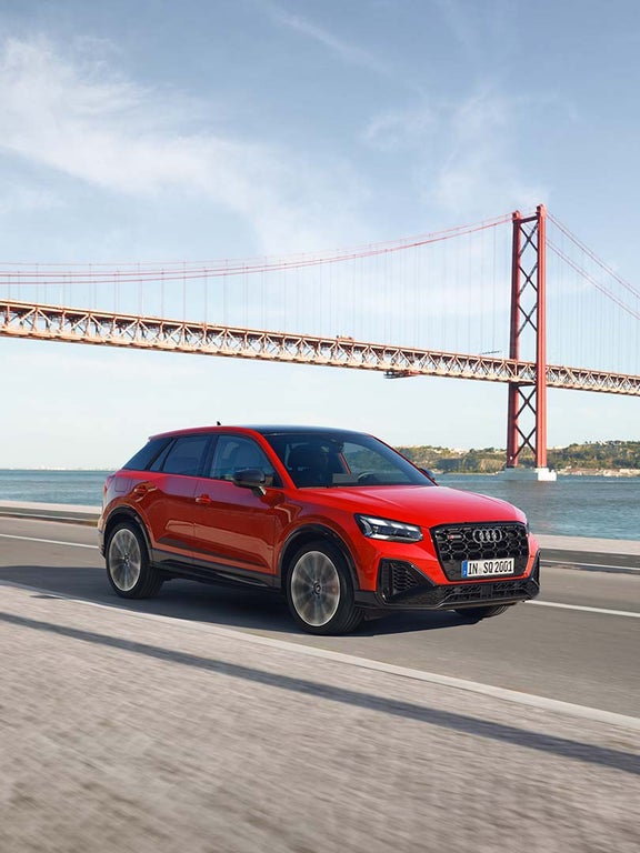 Ein roter Audi SQ2 fährt auf einer Küstenstraße am Meer an roter Hängebrücke entlang.