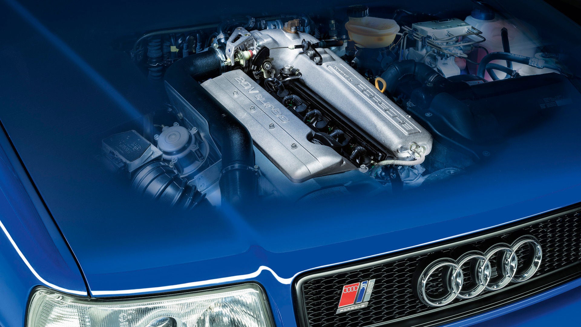 Motorraum eines blauen Audi mit silbernem 20V-Turbo-Motor und sichtbarem Audi-Kühlergrill