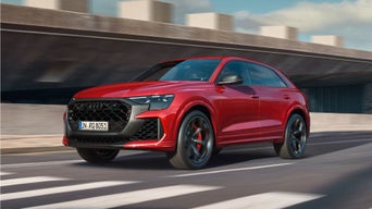 A red Audi RS Q8 SUV performance driving on a road with motion blur, indicating speed